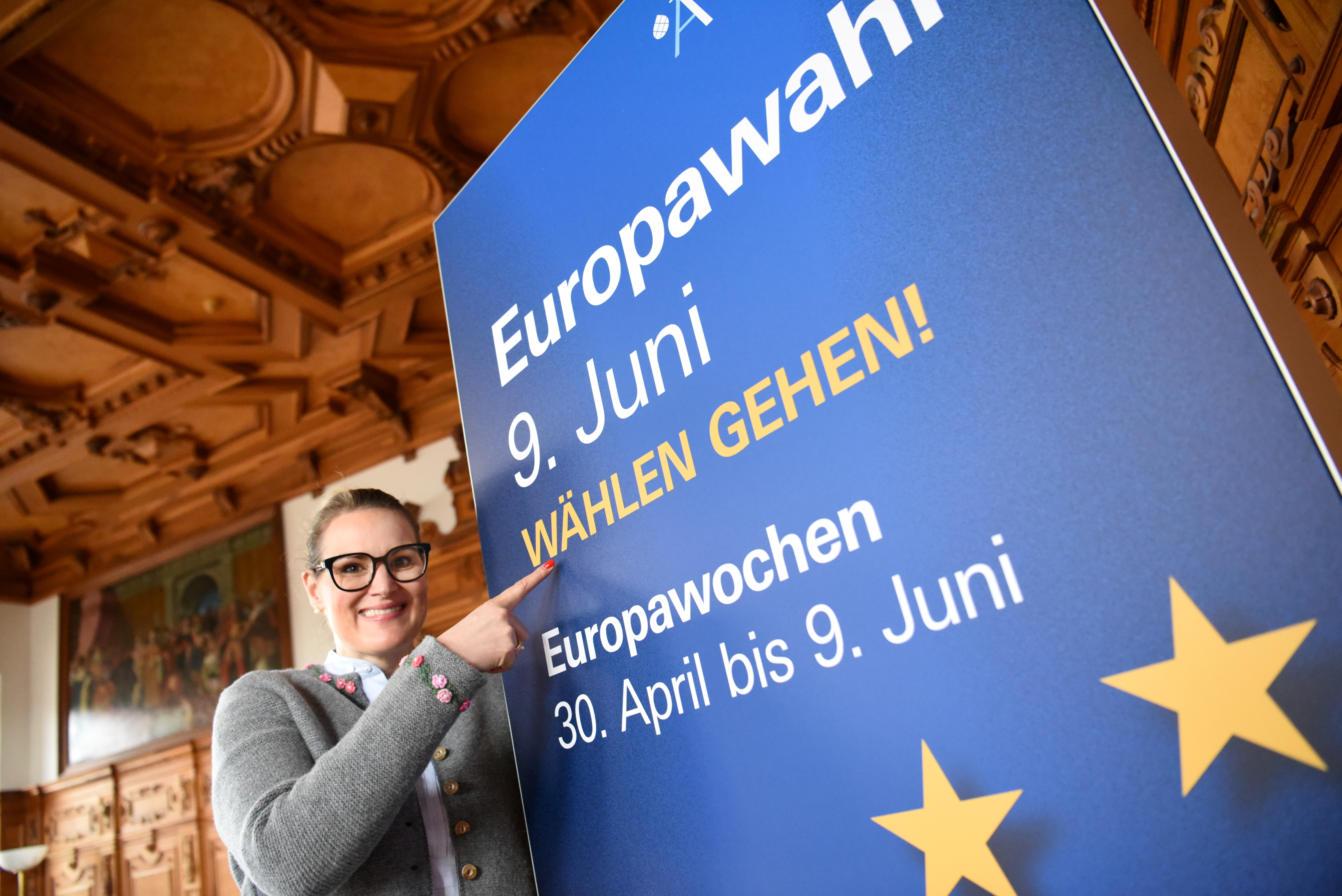 OB Eva Weber zeigt auf ein  Plakat, auf dem steht: "Europawahl 9. Juni, Wählen gehen! Europawochen 30. April bis 9. Juni